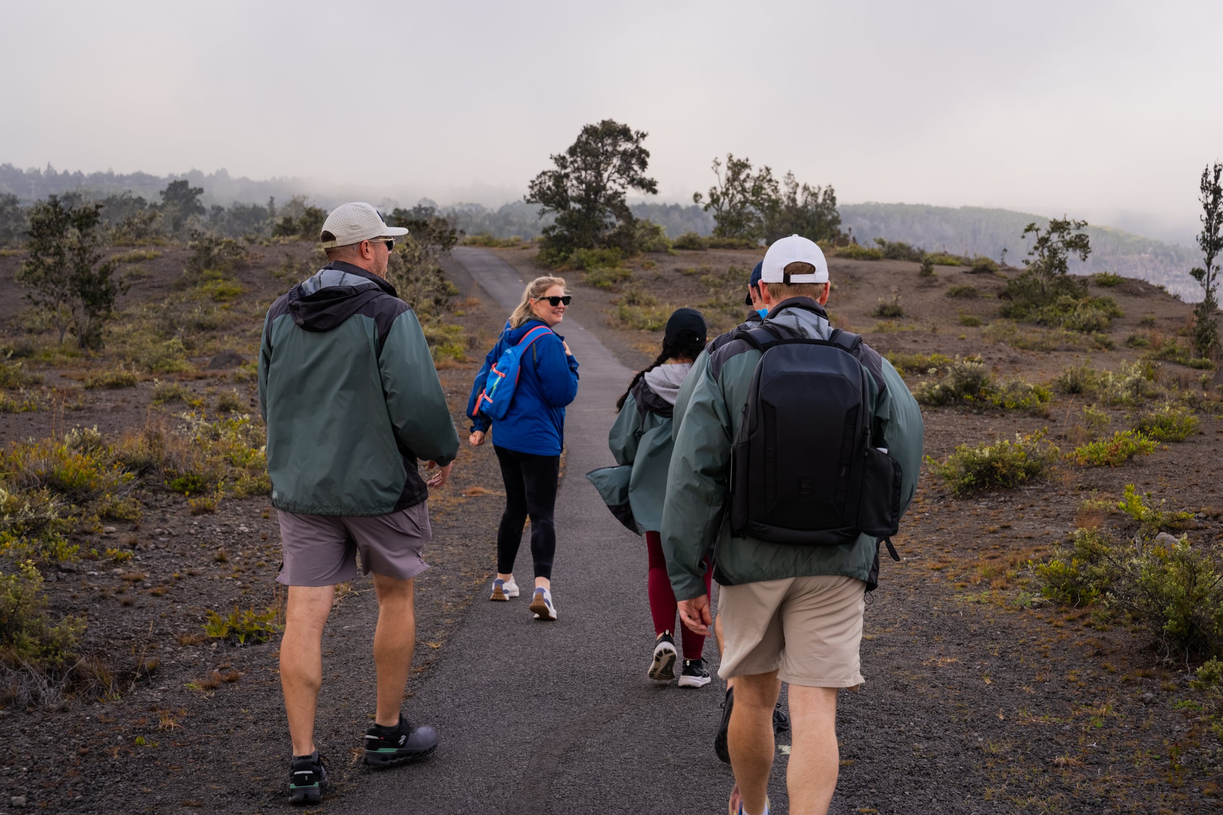 A guided group walking the volcanic ridge trail, fog rolling over the crater beyond